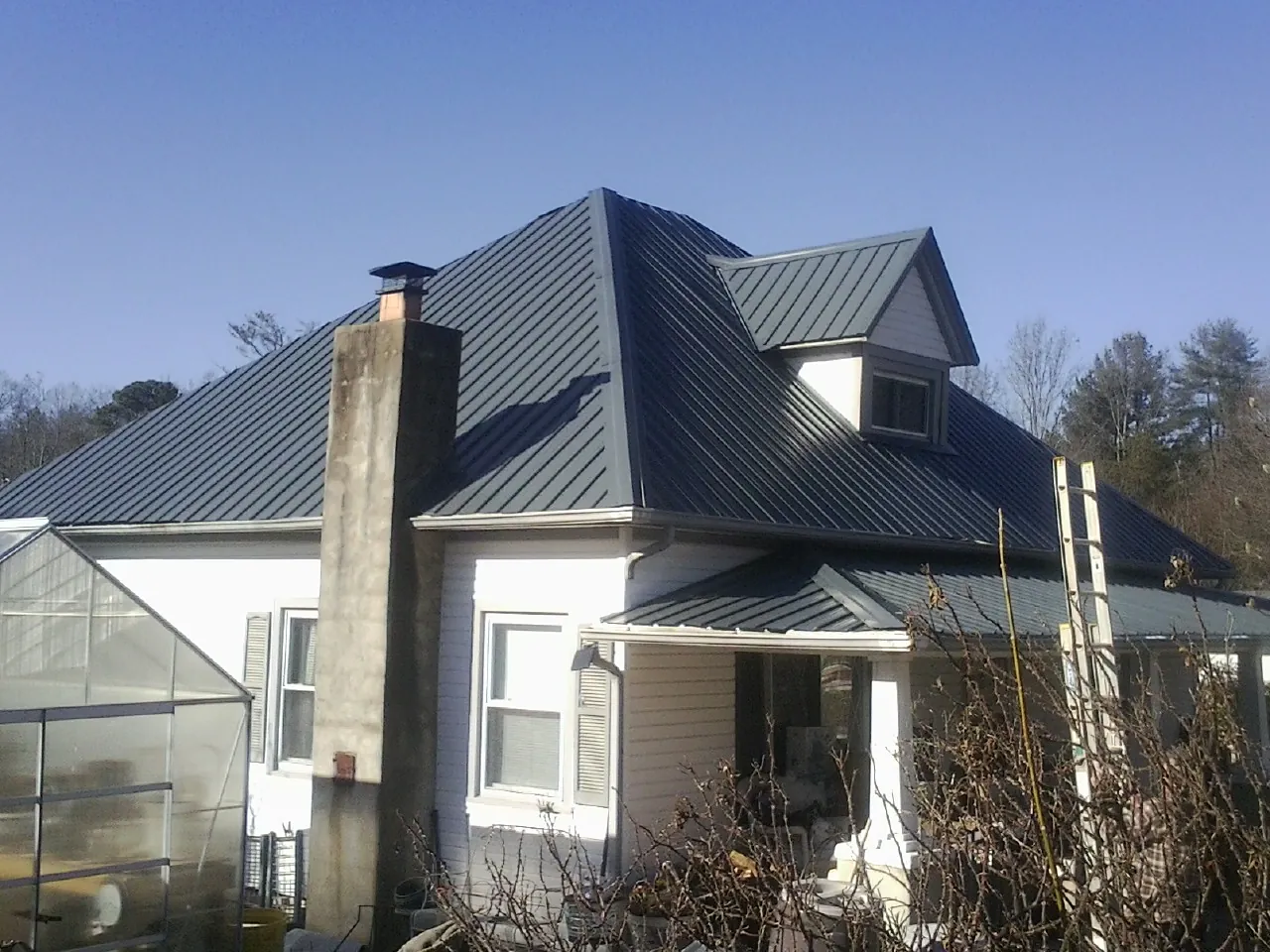 Dark blue standing seam metal roof on a white farmhouse with dormer — Slate & Tile Roof Repair by Roofing Brothers in Livonia