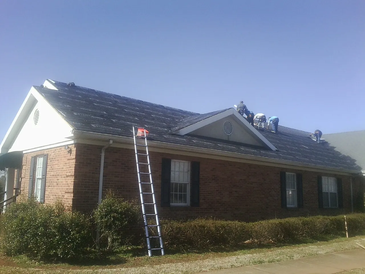 Crew tearing shingles off a brick ranch roof with a ladder set — Metal Roof Repair work by our crew in Livonia