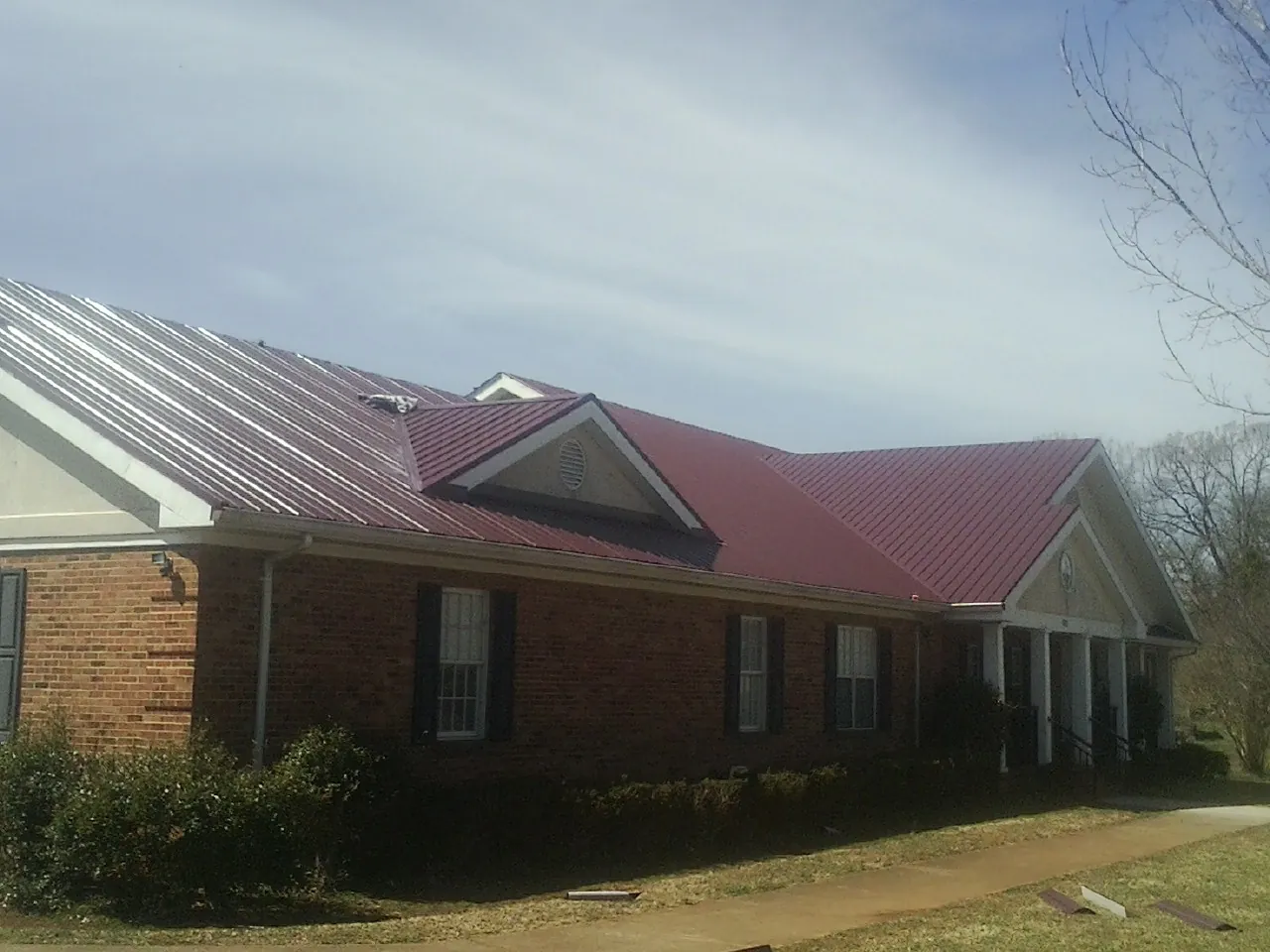 Red metal roof with gabled entries on a long brick building, from a Hail Damage Roof Repair job in Livonia