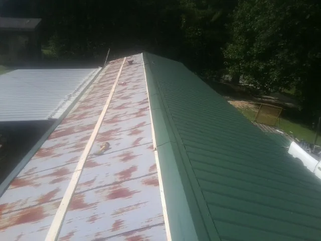 Old rusted panels beside newly installed green metal roofing — Wind Damage Roof Repair by Roofing Brothers in Livonia