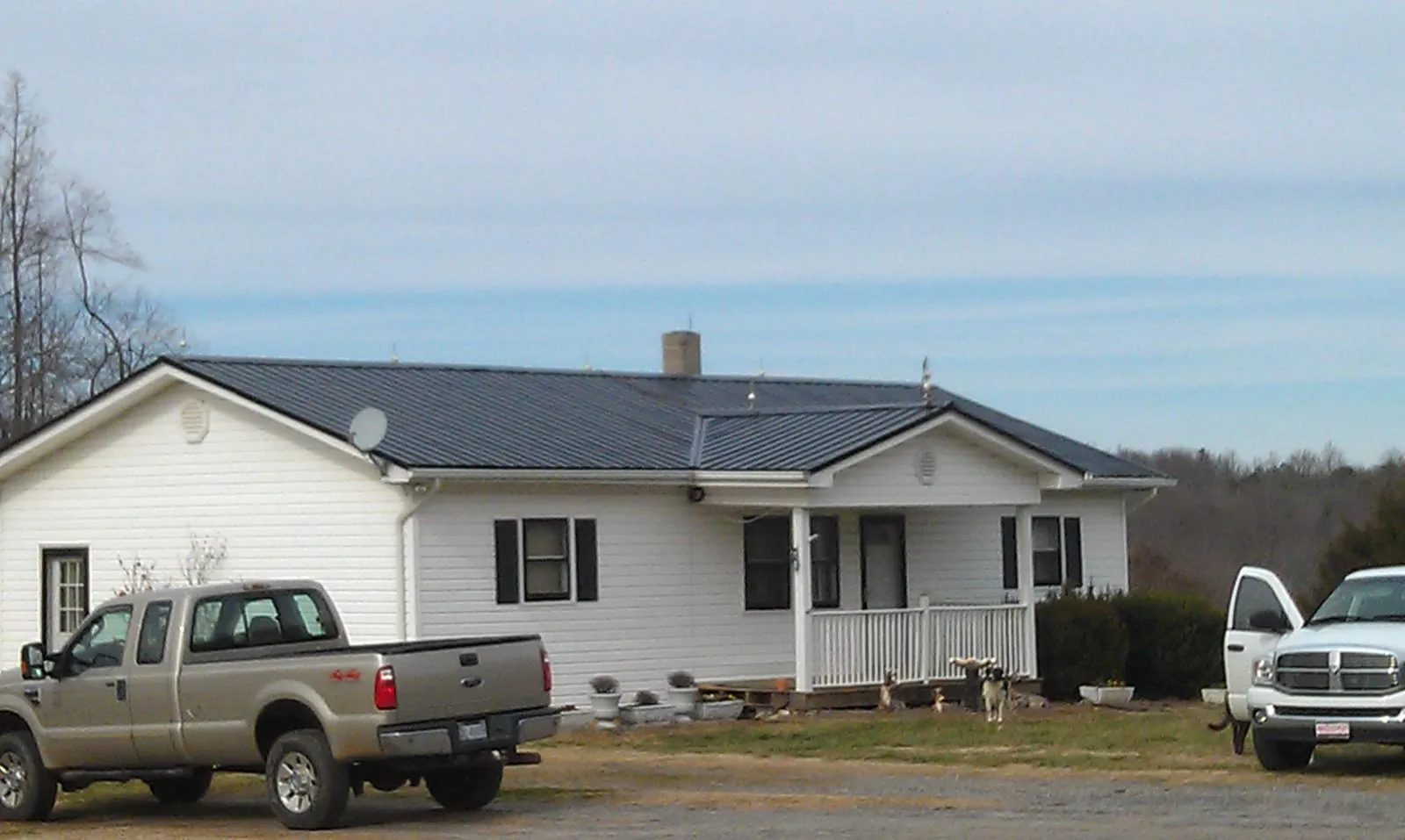 Finished dark metal roof on a white ranch home with work trucks parked in Livonia